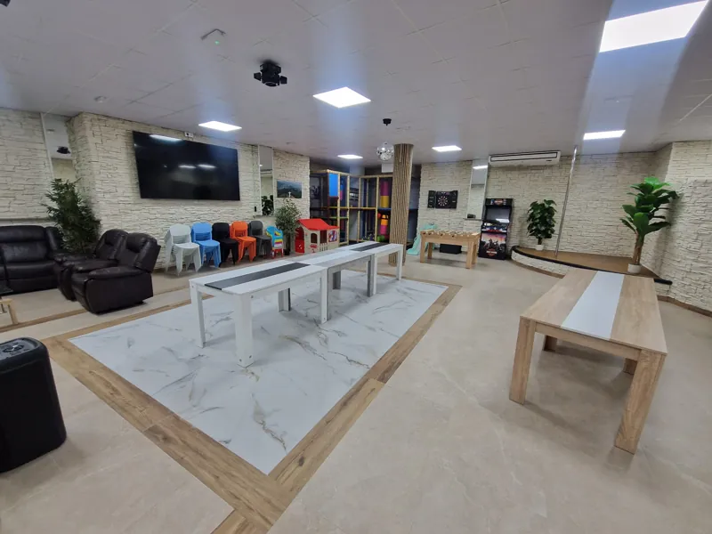 Salón principal con mesas modulares, futbolín, arcade y escenario
